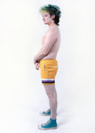 side view of Xander modeling the nonbinary pride boardshort when they were a size 32
